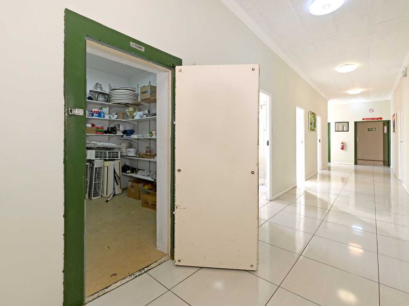 A long tiled hallway featuring multiple doorways and a built-in storage closet with shelving.