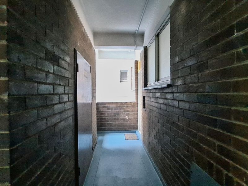 A narrow apartment hallway featuring exposed brick walls and a sliding window, providing access to the unit entrance.
