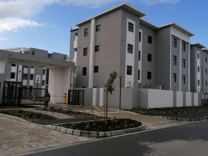 Exterior view of the Ihlathi apartment complex entrance, featuring modern multi-story architecture, secure gated access, perimeter walling with electric fencing, and paved driveway.