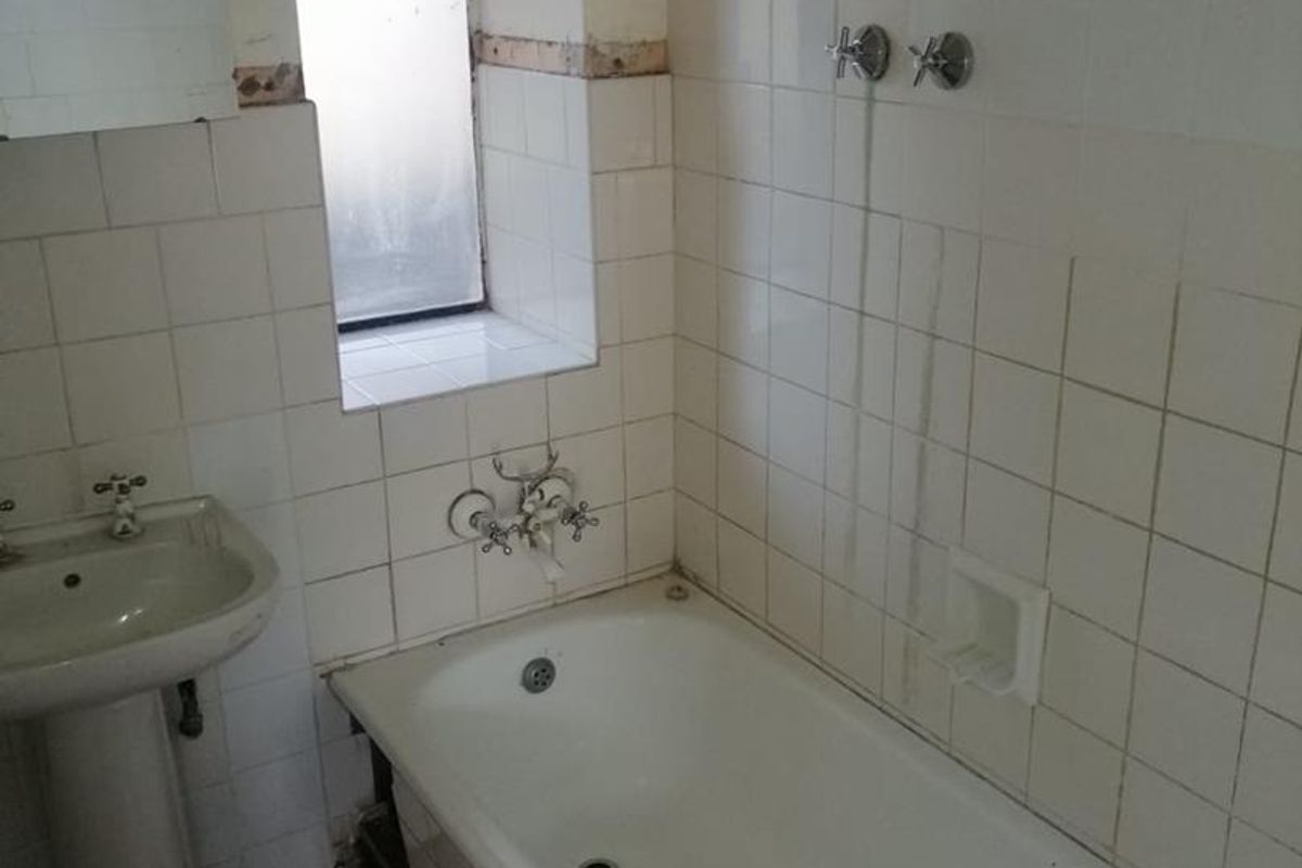 A dated bathroom featuring a pedestal basin and bathtub, requiring renovation due to missing tiles and worn finishes.