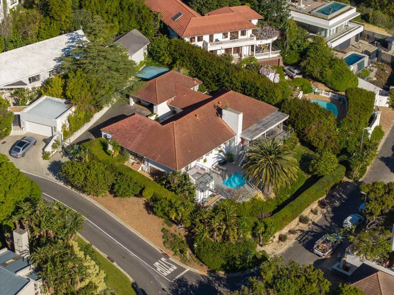 Aerial view of a residential property featuring a tiled roof, private swimming pool, landscaped garden, and paved driveway in a suburban setting.