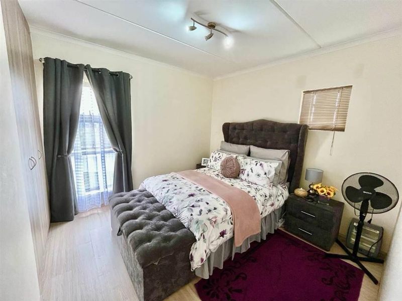 A well-lit bedroom featuring laminate flooring, a built-in wardrobe, and a window with a venetian blind.