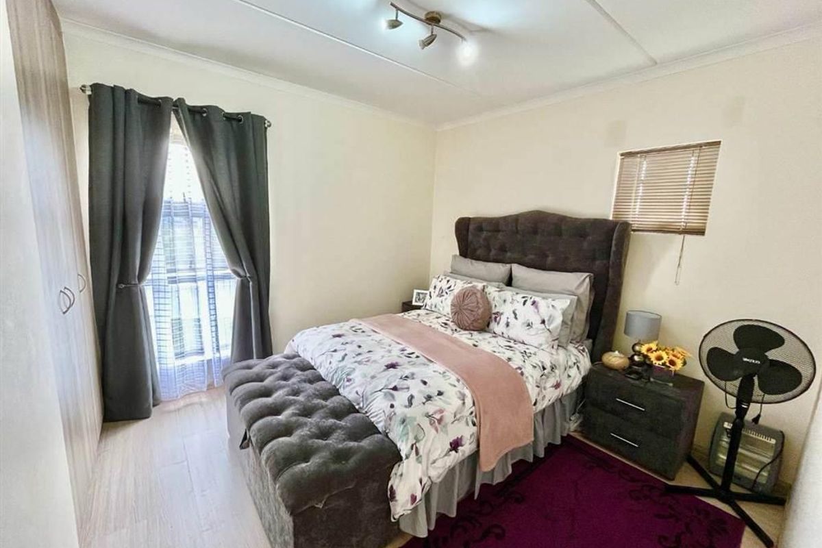 A well-lit bedroom featuring laminate flooring, a built-in wardrobe, and a window with a venetian blind.