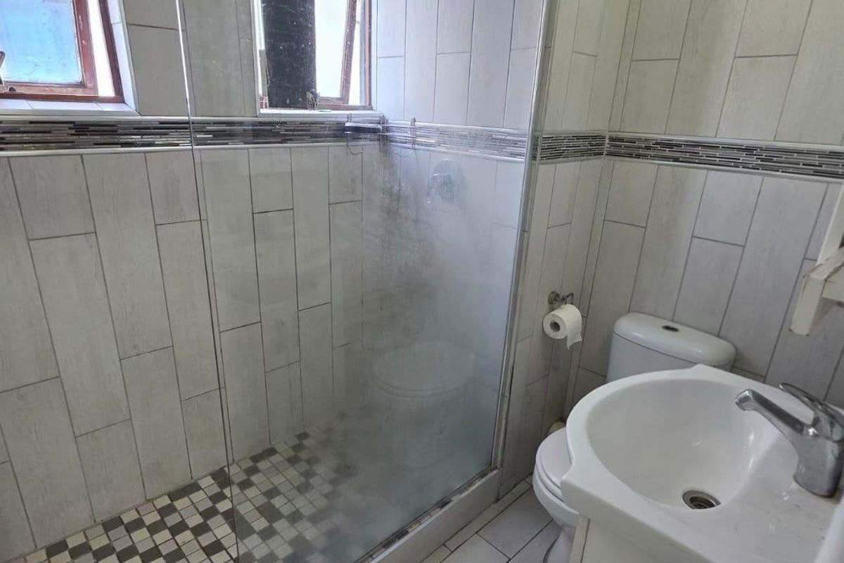 Compact bathroom featuring a glass-enclosed shower, wall-mounted basin, and toilet with neutral wood-look wall tiling and a decorative mosaic border.