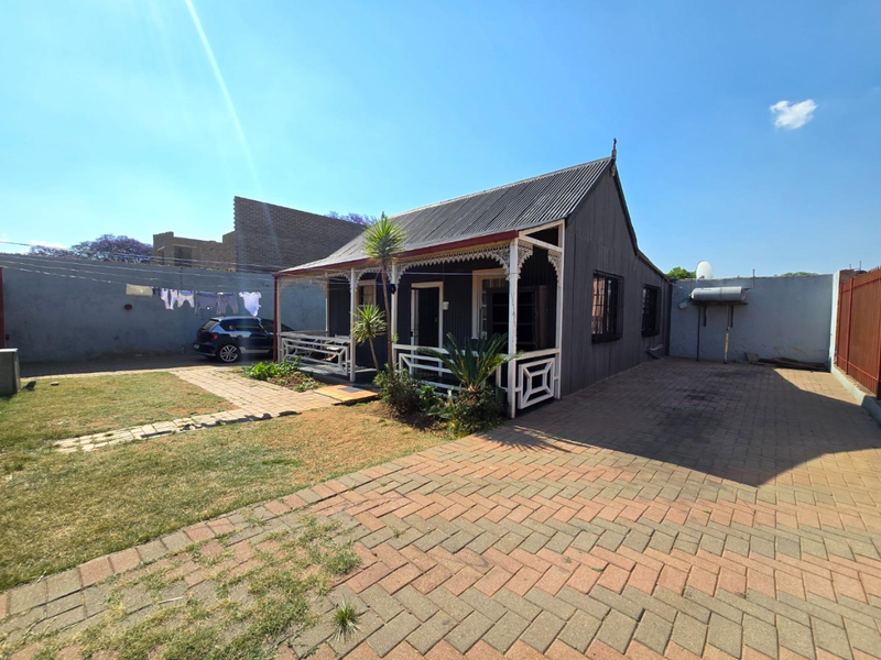 A charming cottage-style home featuring corrugated iron roofing, decorative veranda fretwork, and a paved driveway set within a fenced property.