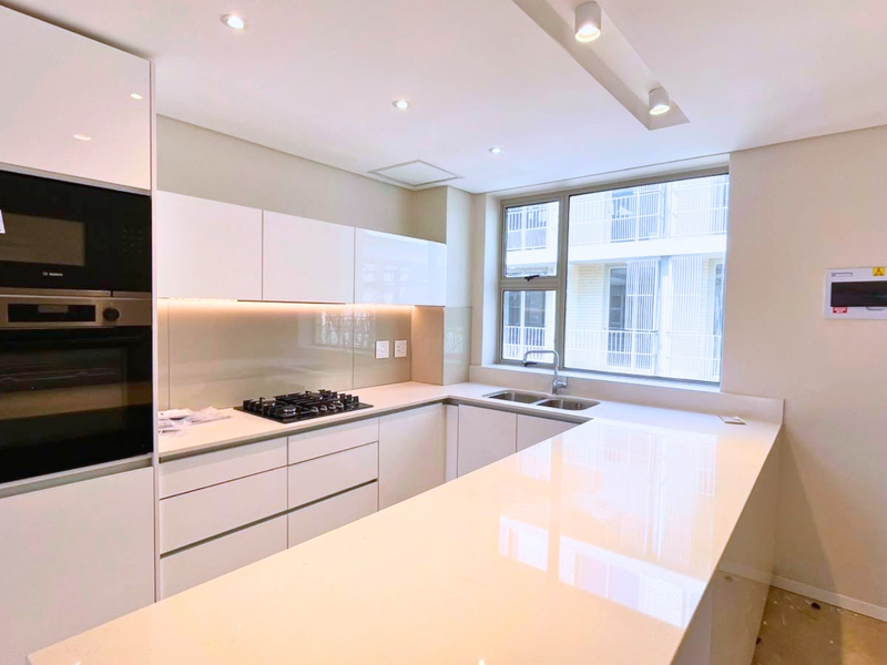 Modern kitchen featuring high-gloss white cabinetry, stone countertops, integrated appliances, and a gas hob, offering a clean and contemporary aesthetic.