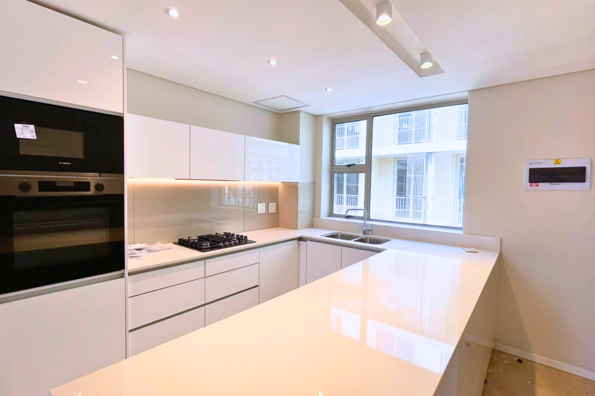 Modern kitchen featuring high-gloss white cabinetry, stone countertops, integrated appliances, and a gas hob, offering a clean and contemporary aesthetic.