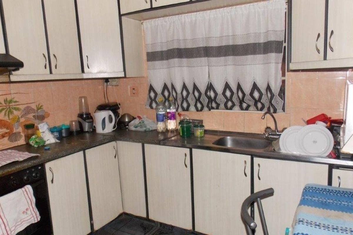 A compact kitchen featuring dated laminate cabinetry, tiled backsplash, built-in oven, and extractor fan, offering potential for a modern renovation.
