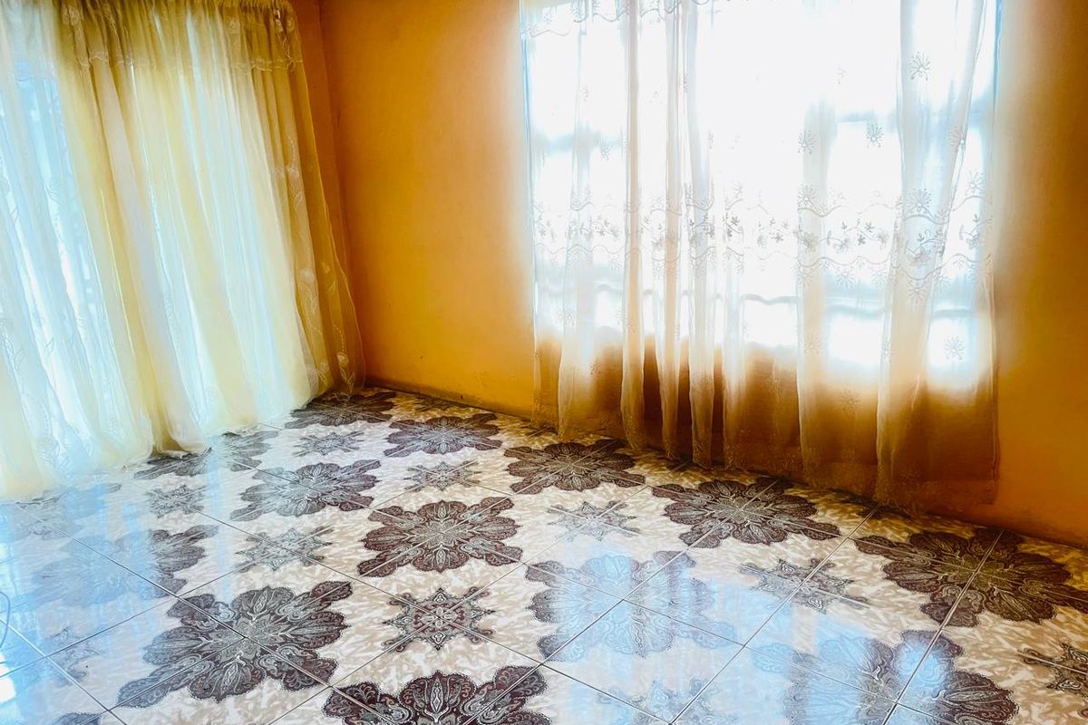 A vacant living room featuring patterned ceramic floor tiles and large windows with curtains, offering a blank canvas for renovation.