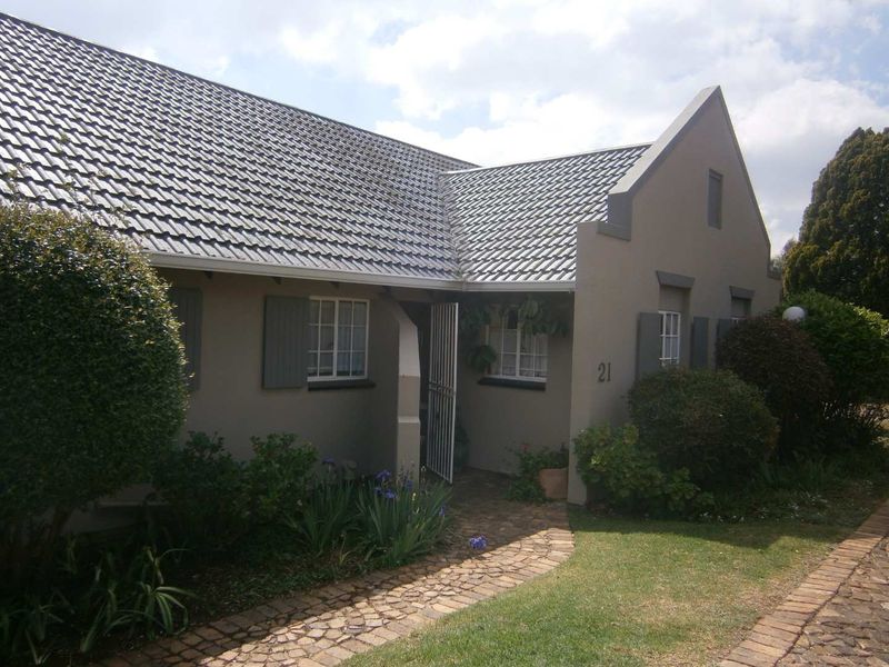 Front elevation of a townhouse featuring a tiled roof, paved walkway, and security gate entrance.