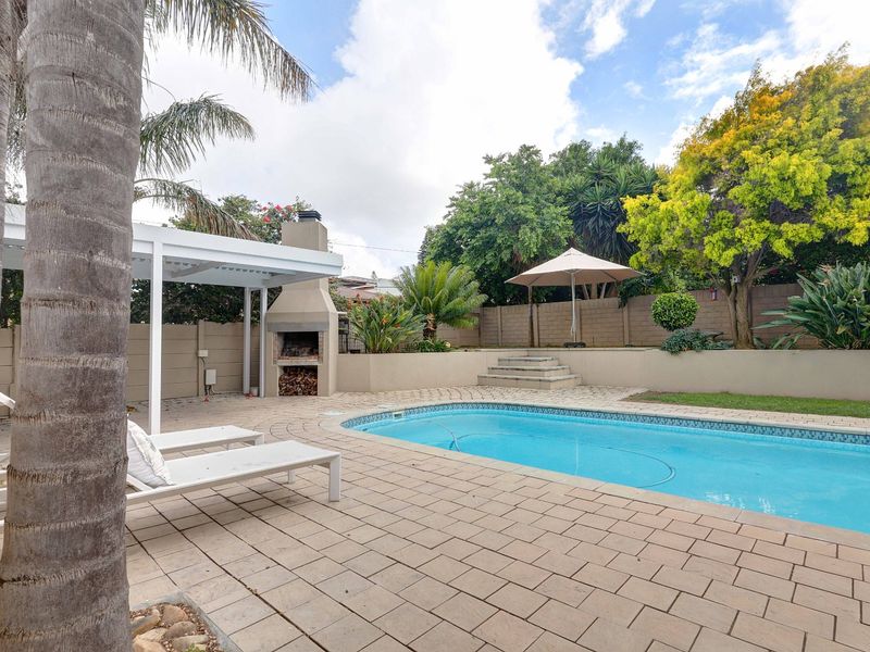 Outdoor pool area featuring a paved patio, built-in braai, pergola, and landscaped garden with retaining walls, perfect for outdoor entertaining.