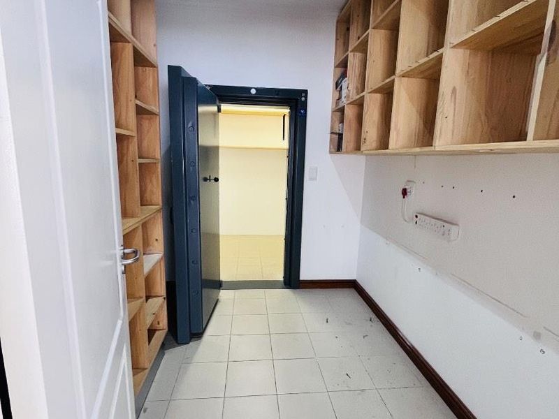 A utility or storage room featuring extensive built-in wooden shelving, tiled flooring, and a secure heavy-duty steel vault door leading to an inner chamber.