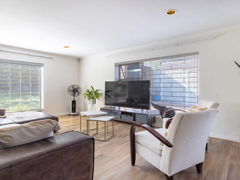 A bright and spacious living room featuring modern laminate flooring, recessed downlighting, and large windows with fitted venetian blinds.