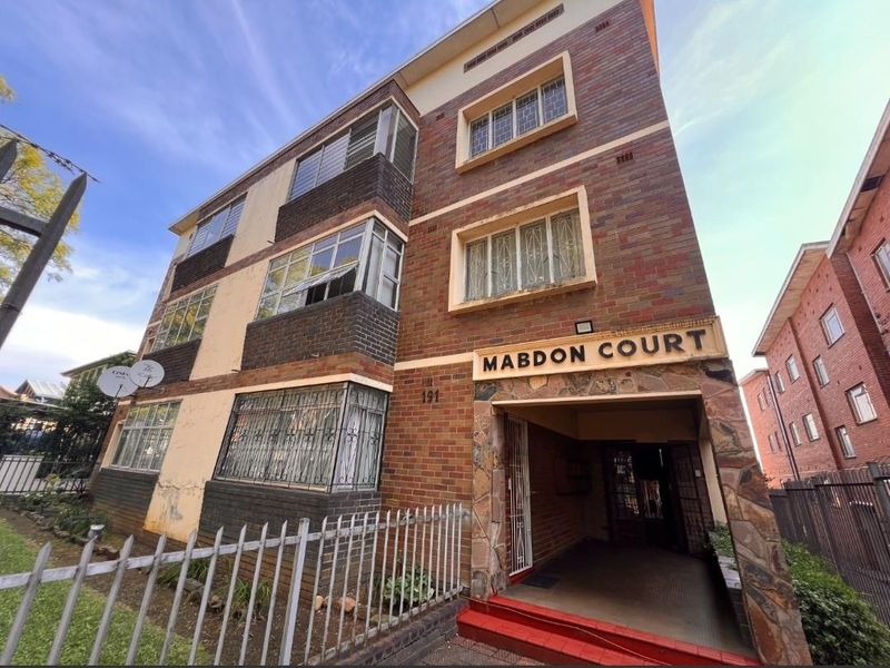 Exterior view of Mabdon Court, a multi-story brick apartment building featuring stone cladding at the entrance and security bars on the windows.