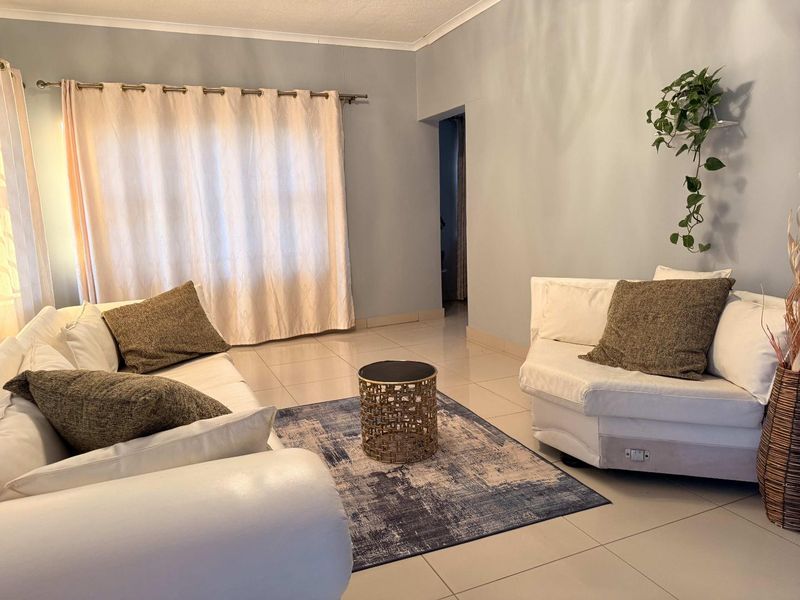 A bright living room featuring neutral tiled flooring and a large window with curtain fixtures, offering a clean and functional space.