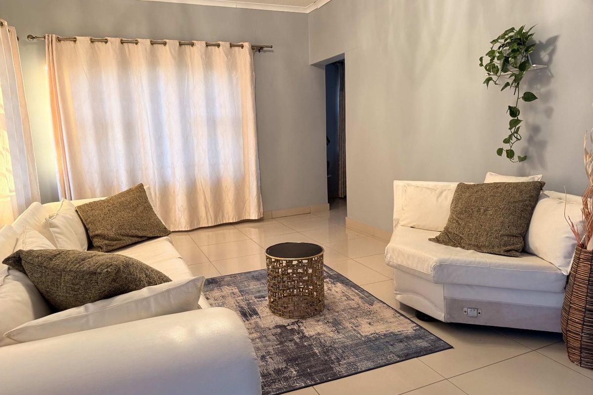 A bright living room featuring neutral tiled flooring and a large window with curtain fixtures, offering a clean and functional space.