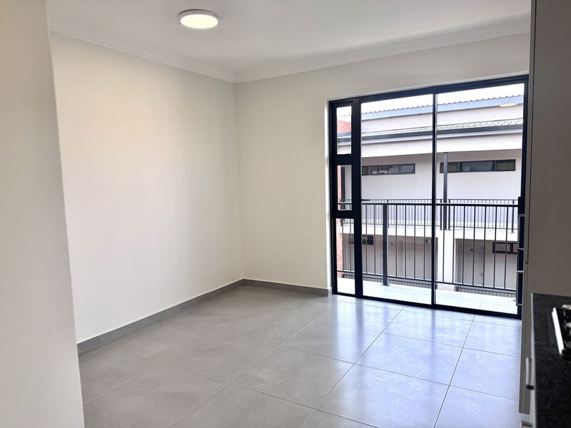 A bright, empty living area featuring modern grey floor tiles, neutral walls, and a large sliding glass door leading to a private balcony.