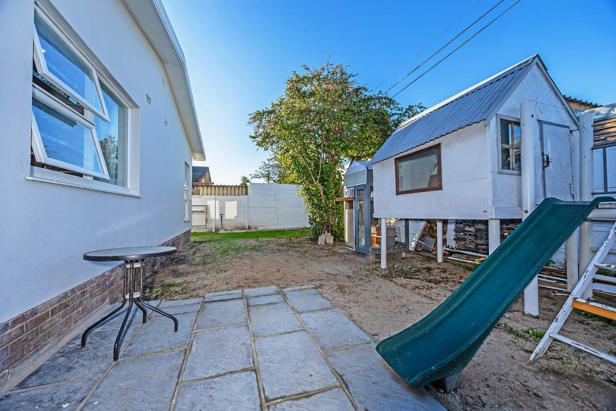 Rear garden area featuring a stone paved patio, raised playhouse structure, and perimeter boundary walling.