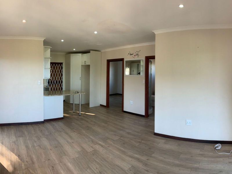 Spacious open-plan living area featuring laminate flooring, recessed lighting, and a functional kitchen nook with built-in cabinetry and a breakfast counter.