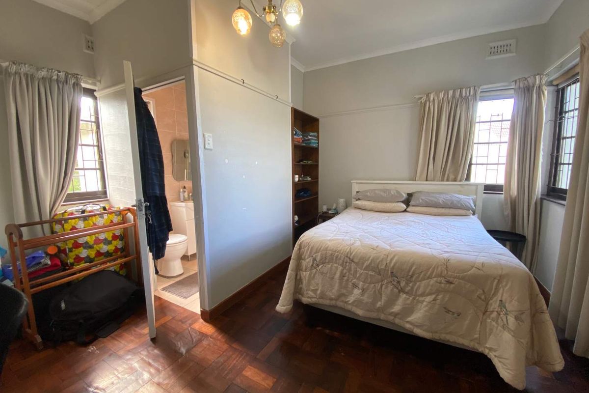 A bedroom featuring parquet flooring, built-in shelving, and an attached en-suite bathroom with security bars on the windows.