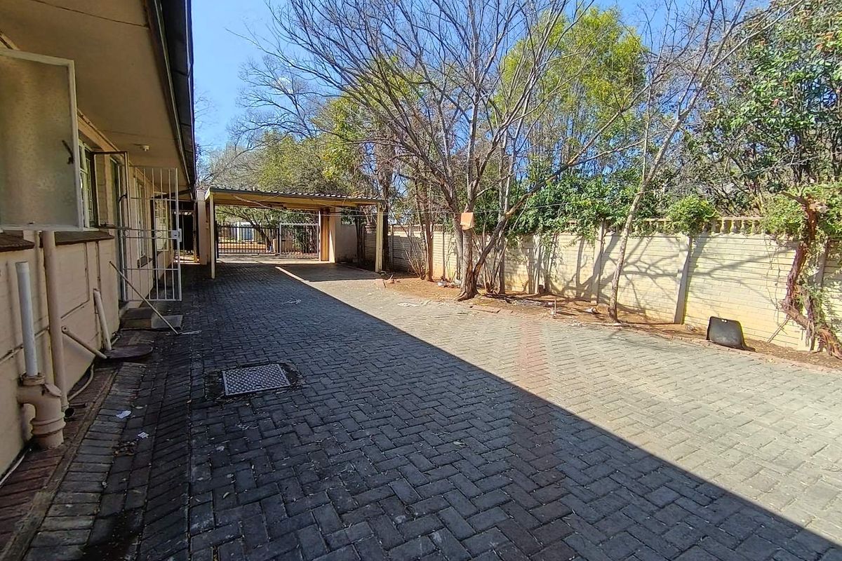 A paved rear driveway area featuring a carport, perimeter walling, and security gate access.