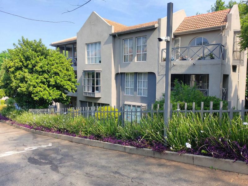 A multi-story townhouse exterior featuring a stucco facade, terracotta roof tiles, and a secure metal-fenced garden area.