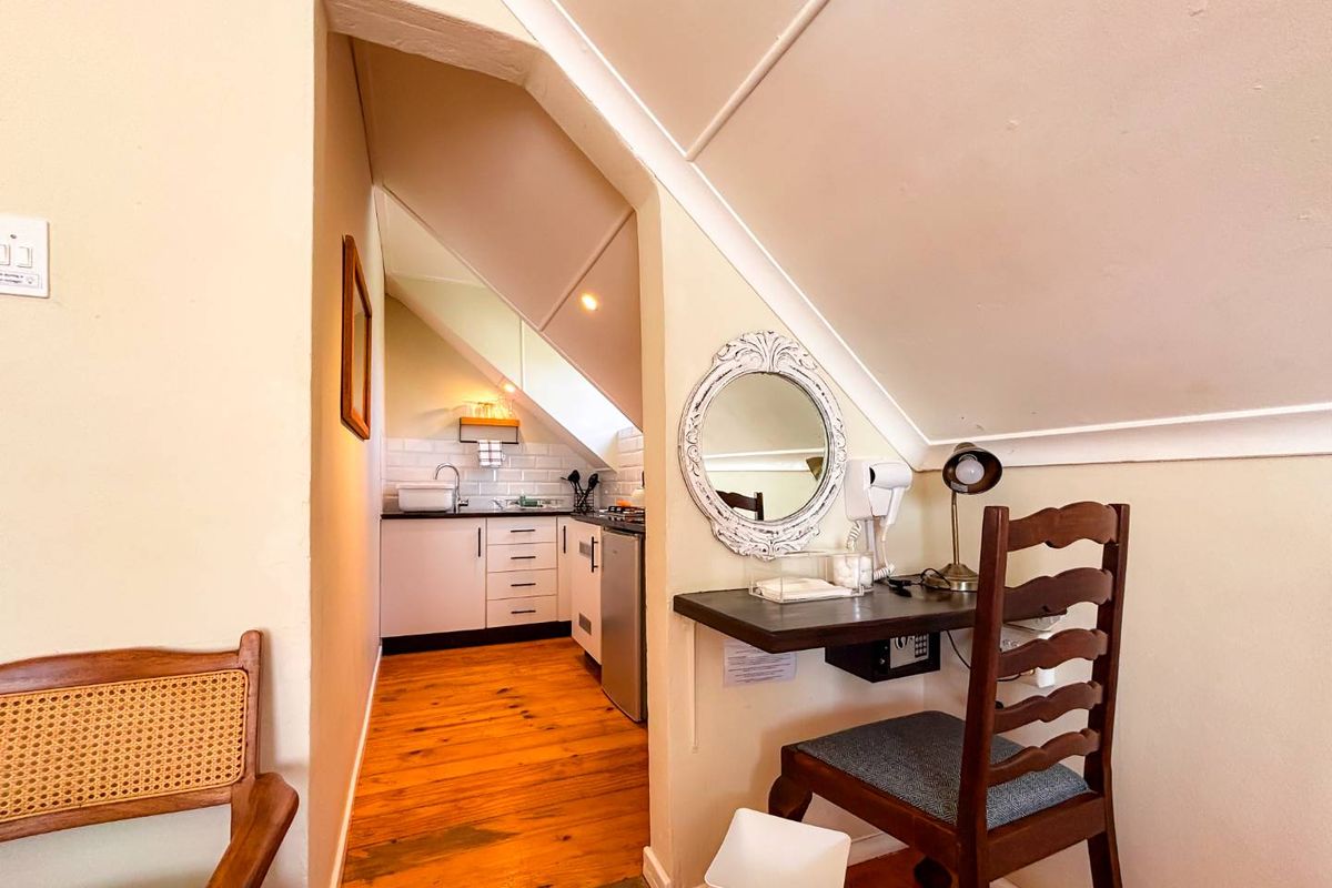 A compact kitchen area featuring white cabinetry, subway tile backsplash, and hardwood flooring, adjacent to a built-in desk space under a sloped ceiling.