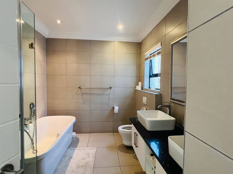 Modern bathroom featuring a freestanding bathtub, glass-enclosed shower, and a sleek vanity with double vessel sinks and granite countertops.