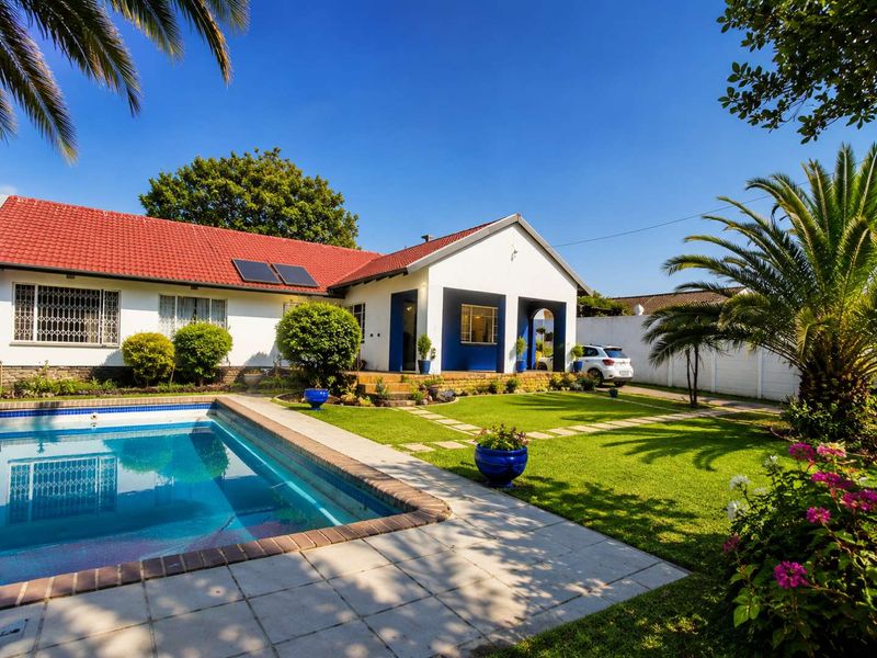 Rear view of the property featuring a well-maintained swimming pool, landscaped garden, paved patio area, and solar panels on the tiled roof.