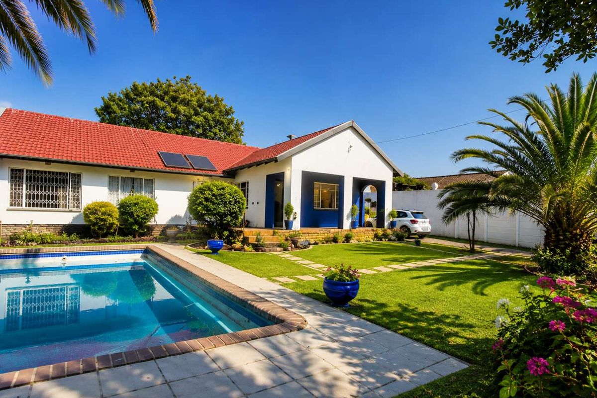 Rear view of the property featuring a well-maintained swimming pool, landscaped garden, paved patio area, and solar panels on the tiled roof.