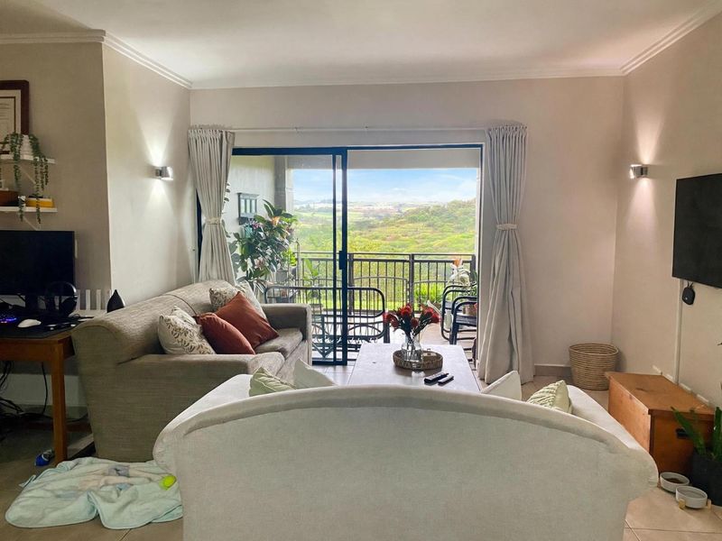 A comfortable living room featuring tiled floors, wall-mounted lighting, and large sliding glass doors that open onto a balcony with scenic views.