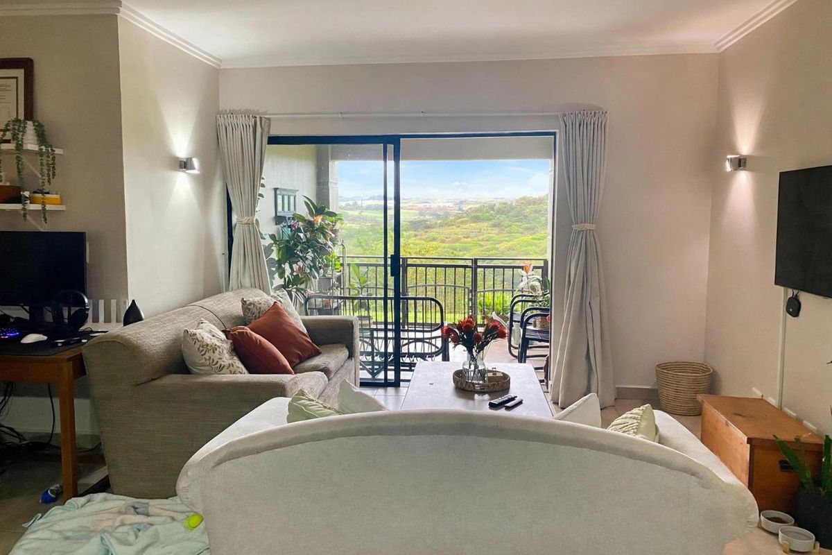 A comfortable living room featuring tiled floors, wall-mounted lighting, and large sliding glass doors that open onto a balcony with scenic views.