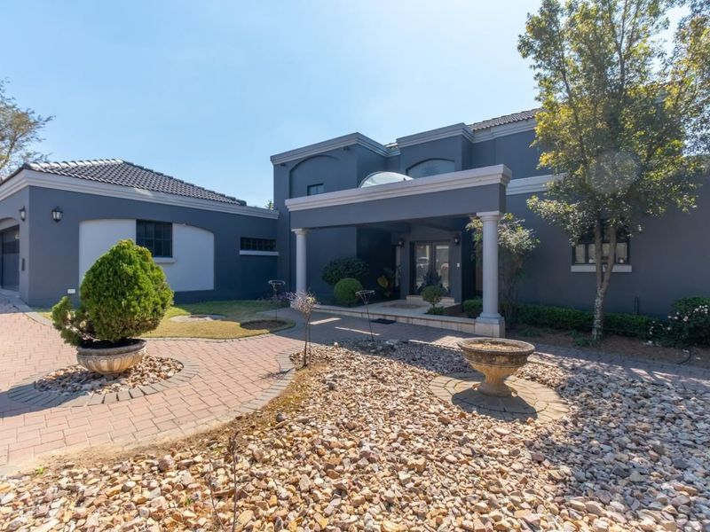 A well-maintained front exterior featuring a paved driveway, covered entrance porch with columns, and a landscaped garden area.