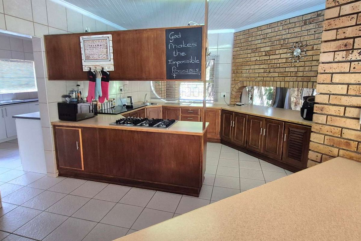 A spacious kitchen featuring wooden cabinetry, a built-in gas hob, and a breakfast counter, with an adjacent scullery area visible.