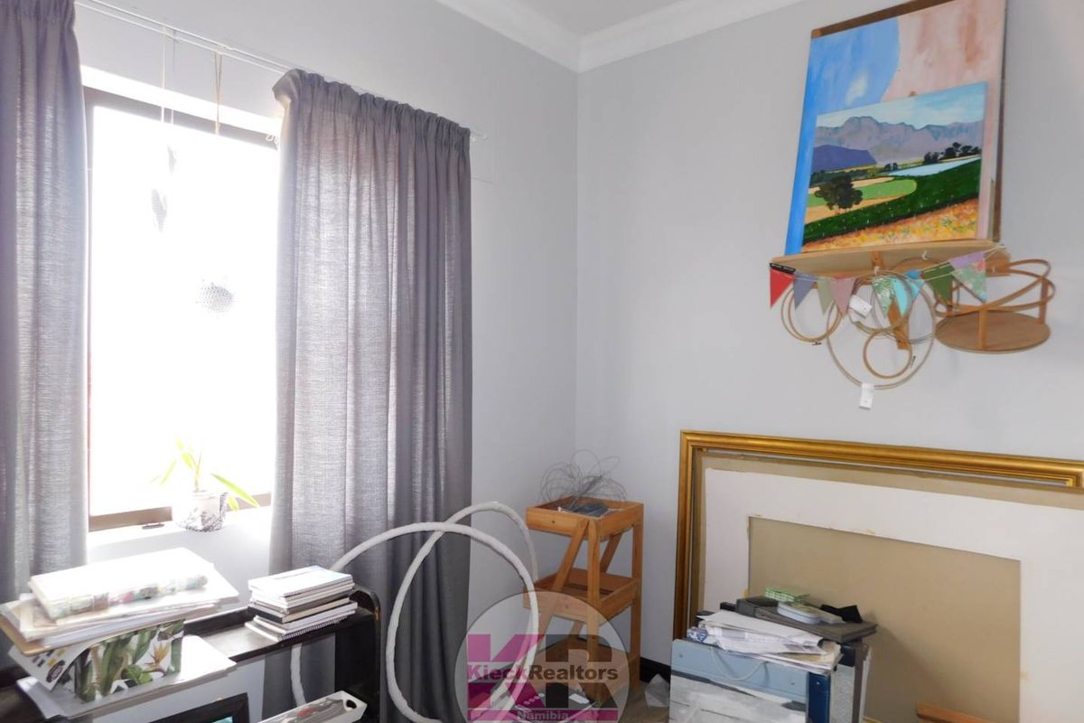 A bedroom featuring neutral wall paint, crown molding, and a window with curtains.