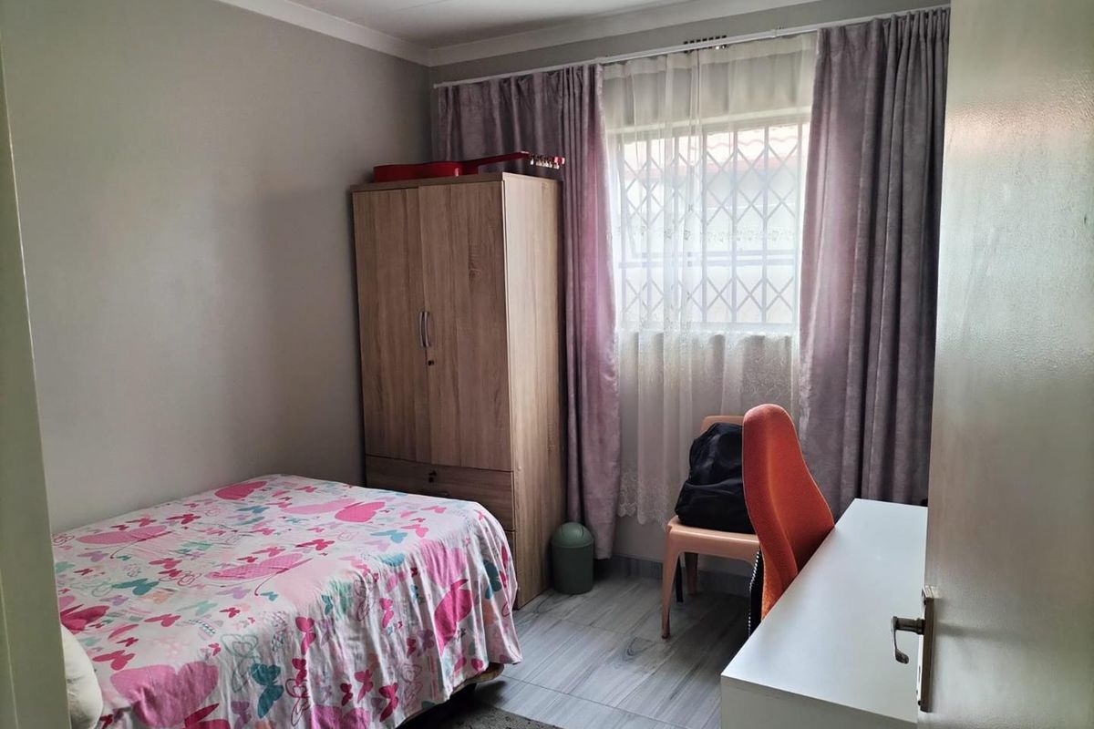 A functional bedroom featuring tiled flooring, a window with security bars, and neutral wall finishes.