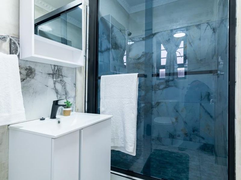Modern bathroom featuring a sleek vanity, marble-look wall tiling, and a contemporary glass-enclosed shower with black framing.