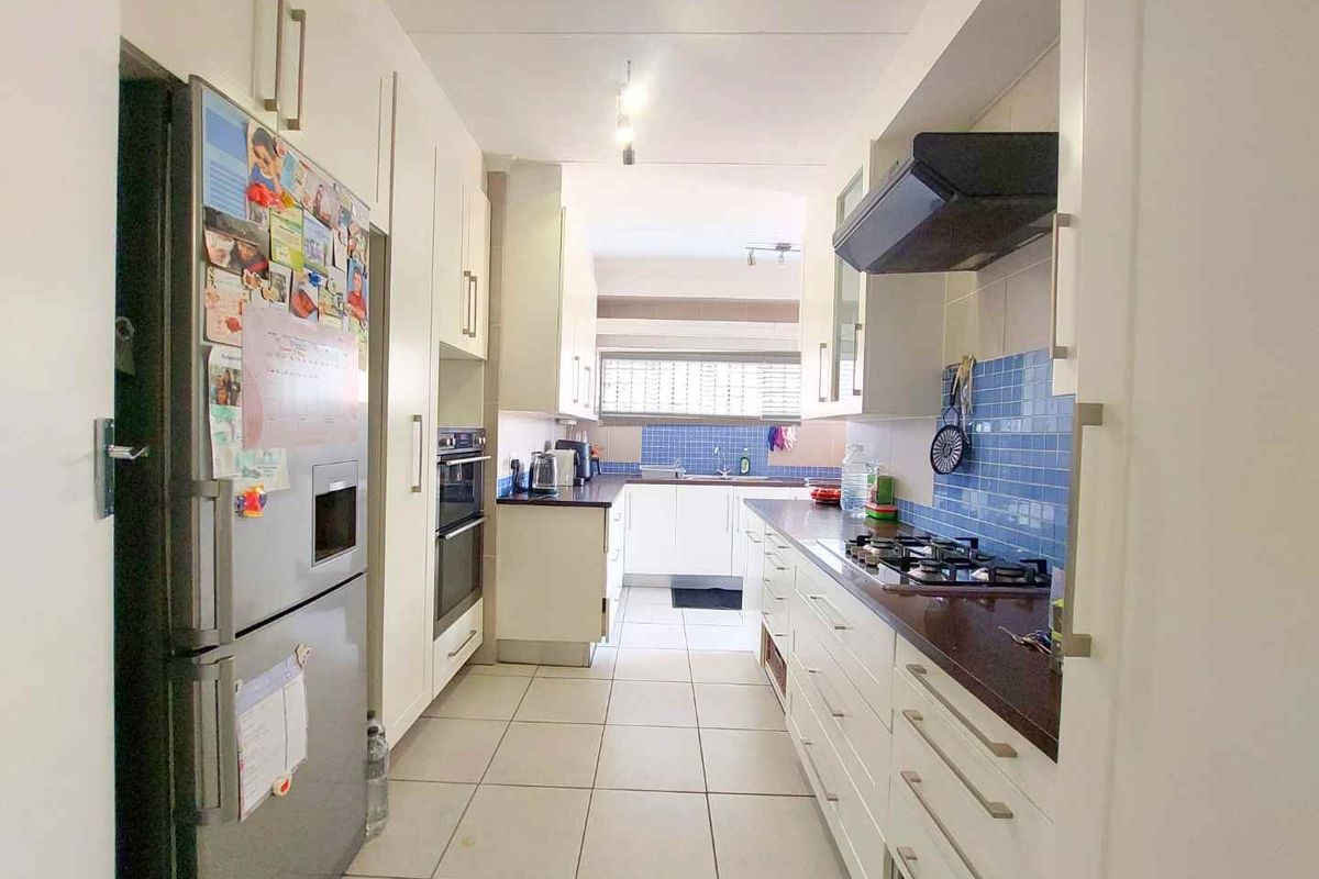 A functional galley-style kitchen featuring white cabinetry, dark countertops, a built-in oven, and a gas hob with an extractor fan.