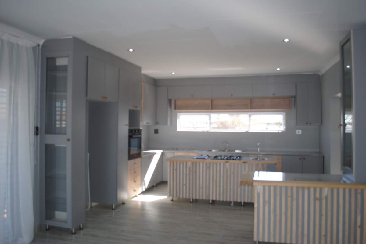 Modern kitchen featuring grey cabinetry, a central island with a built-in gas hob, and integrated oven, set against a neutral backdrop.