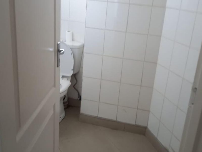 A compact bathroom featuring white wall tiles and tiled flooring, currently in a basic, dated condition.