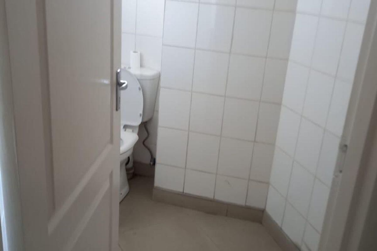 A compact bathroom featuring white wall tiles and tiled flooring, currently in a basic, dated condition.