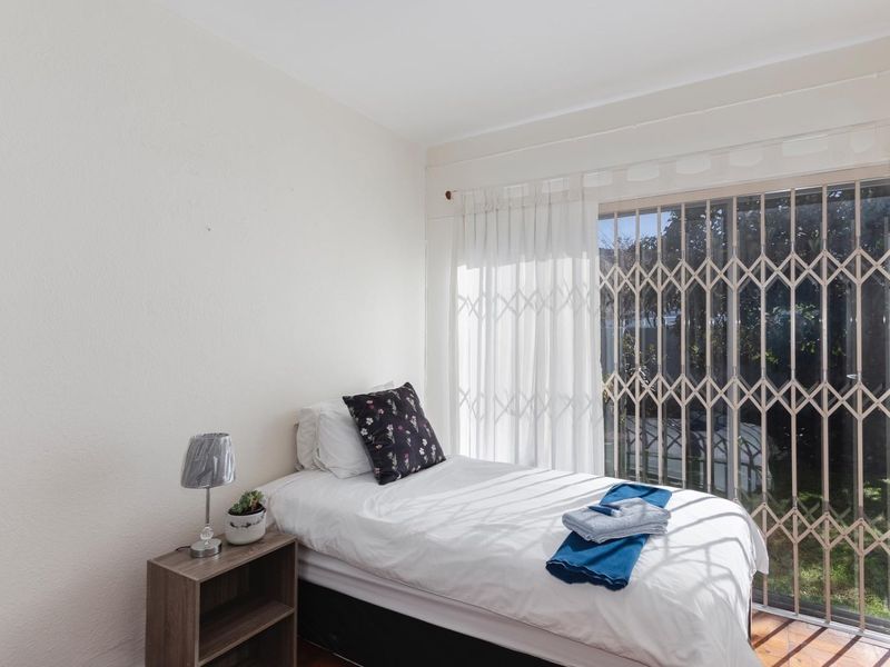 A bedroom featuring wooden flooring and a sliding glass door with a security gate, providing access to the exterior.