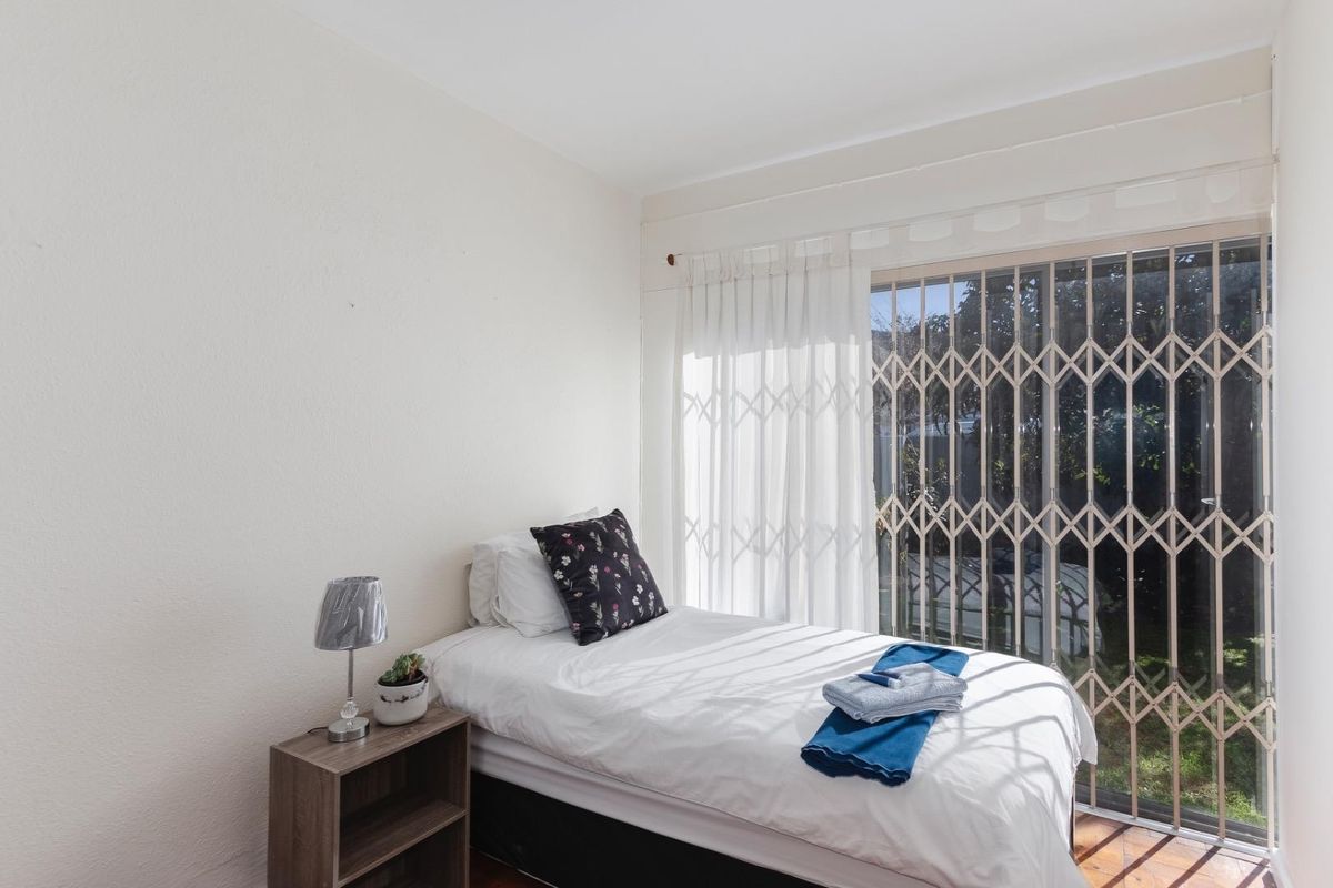 A bedroom featuring wooden flooring and a sliding glass door with a security gate, providing access to the exterior.