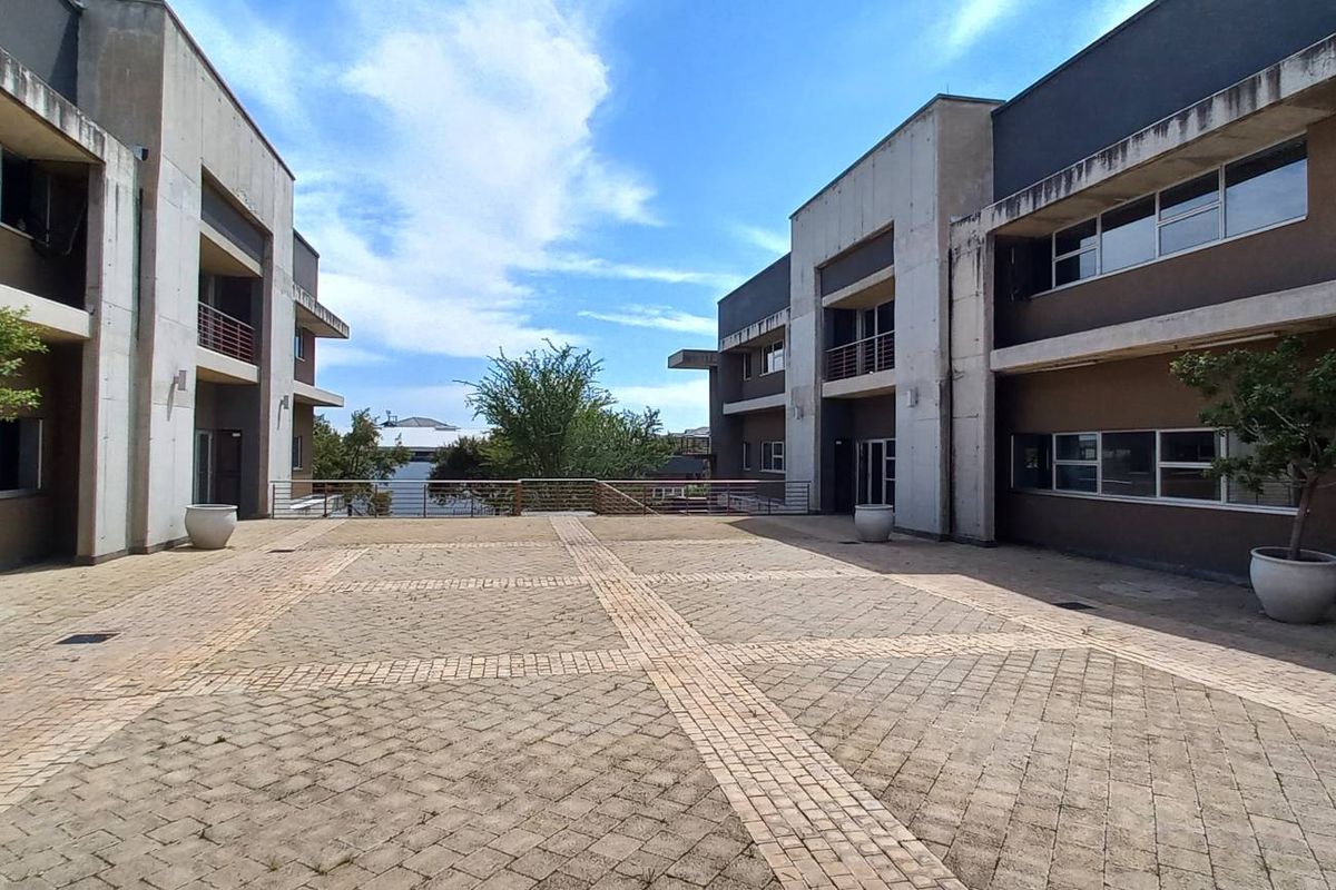 A spacious paved courtyard situated between two modern office building wings, featuring concrete architectural elements and metal balcony railings.
