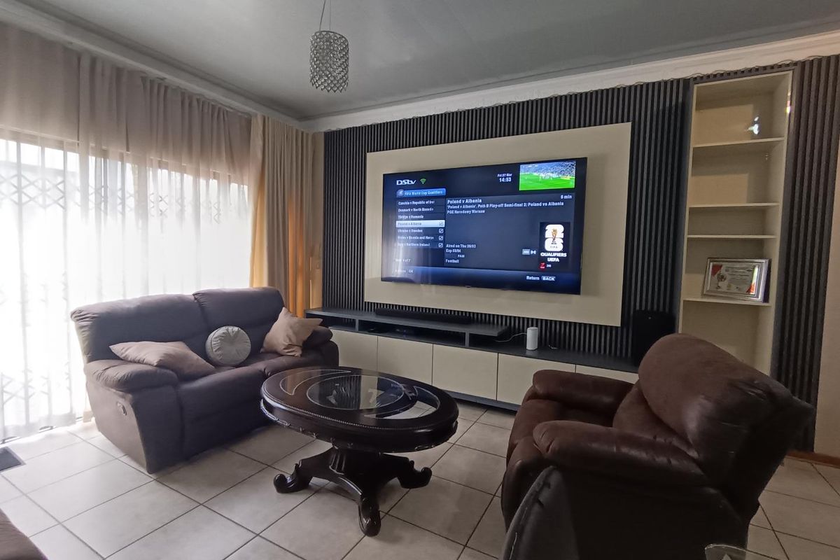 A comfortable living room featuring a custom built-in media wall with integrated shelving, tiled flooring, and large windows with curtain treatments.