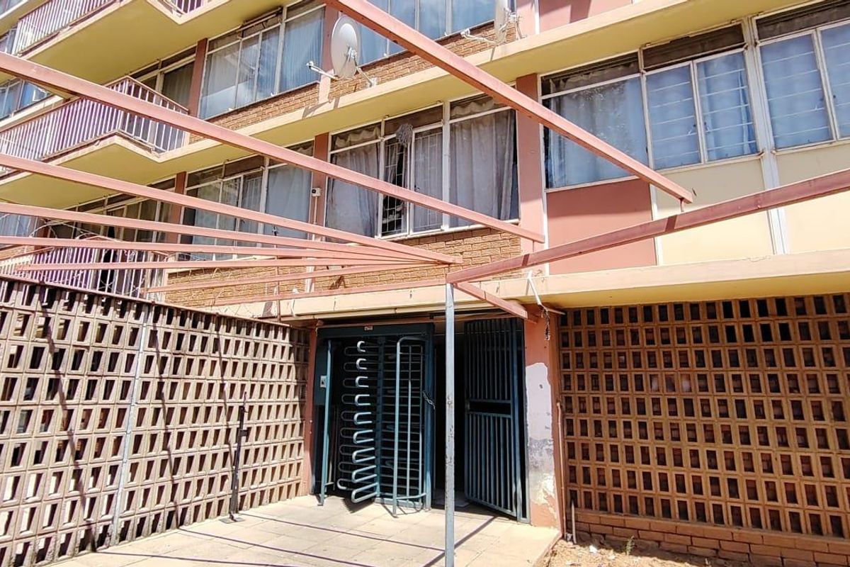 Rear exterior view of the apartment building featuring a paved patio area, breeze block privacy walls, and metal security gate access.