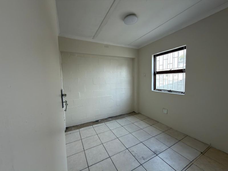 An empty bedroom featuring tiled flooring, a window with security bars, and a painted masonry feature wall.