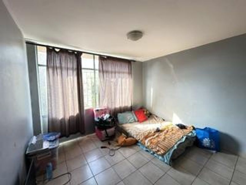 A bedroom featuring tiled flooring and a large window, providing natural light. The space requires cosmetic updates to the wall finishes.