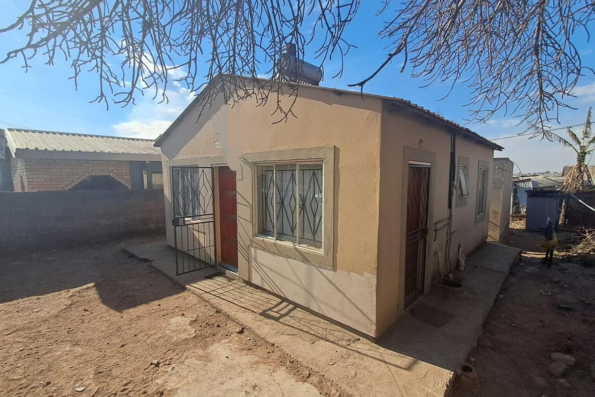 Front view of a single-story detached house featuring a solar water heater, security gates, and a concrete perimeter apron.