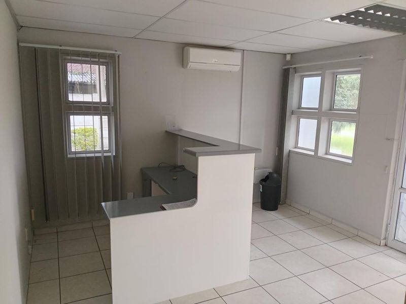 A functional office space featuring a built-in reception desk, tiled flooring, suspended ceiling, and a wall-mounted air conditioning unit.